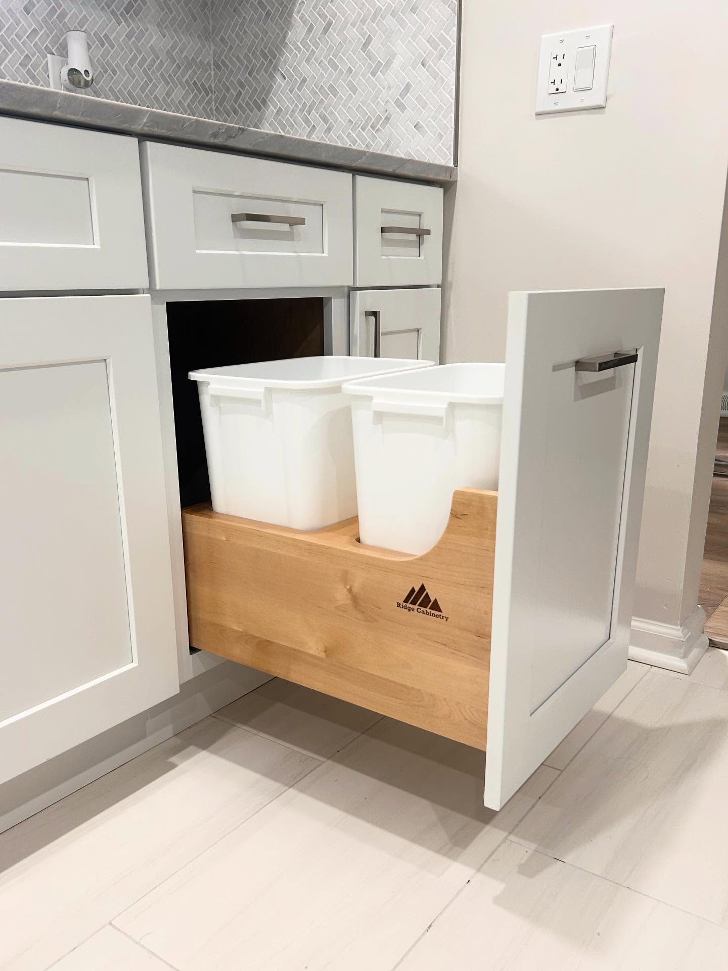Open white Shaker cabinet with a wood pull-out drawer holding two waste bins